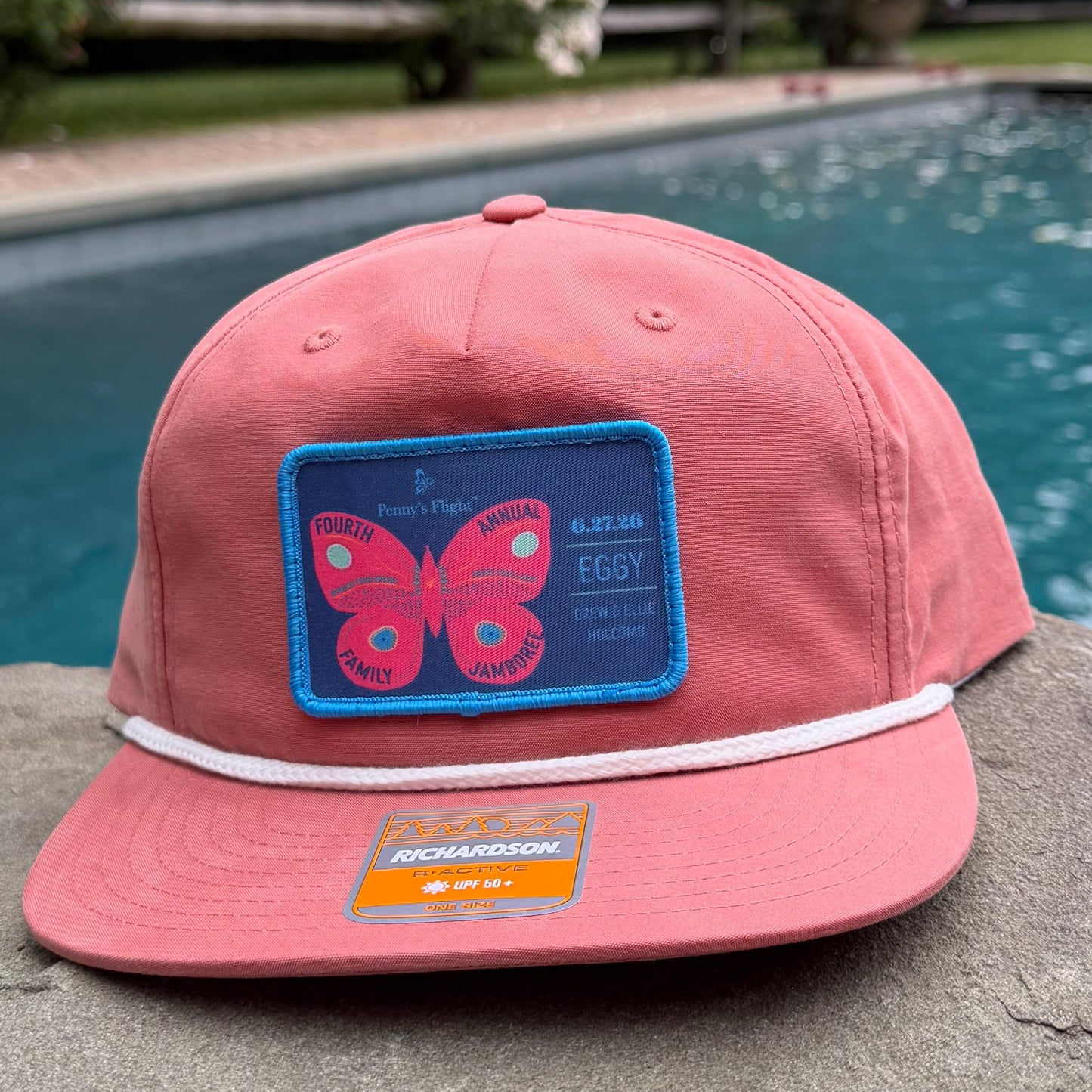 Pink cap with a blue logo leaning against a concrete wall by a poolside.